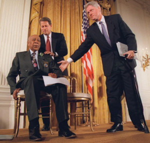 President Clinton and Vice President Al Gore, back, help Herman Shaw, 94, a Tuskegee Syphilis Study victim, during a news conference Friday, May 16, 1997. Making amends for a shameful U.S. experiment, Clinton apologized to Black men whose syphilis went untreated by government doctors.                            (AP Photo/Doug Mills) 